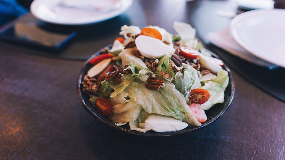 A bowl of salad with lettuce, cherry tomatoes and pecans