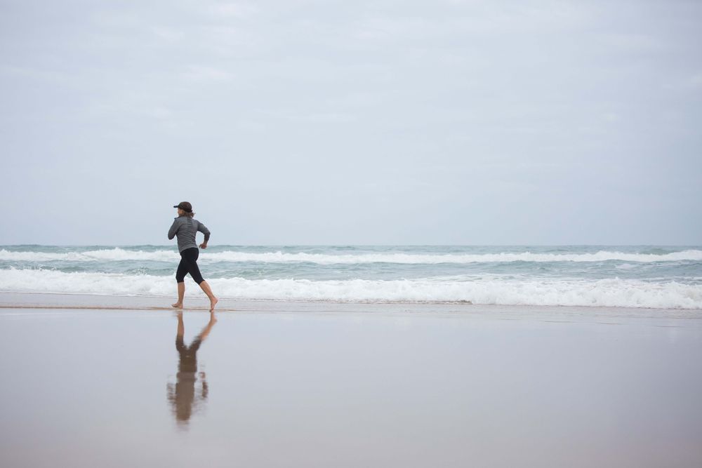A woman running barefoot along the shore on an overcast day